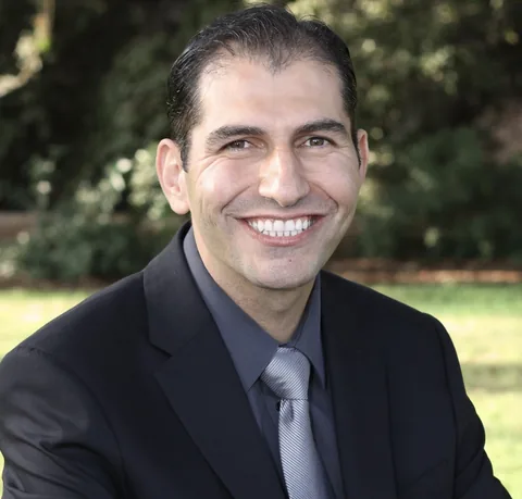 Portrait of Dr. Feras Al Rezk smiling, wearing a dark suit and tie