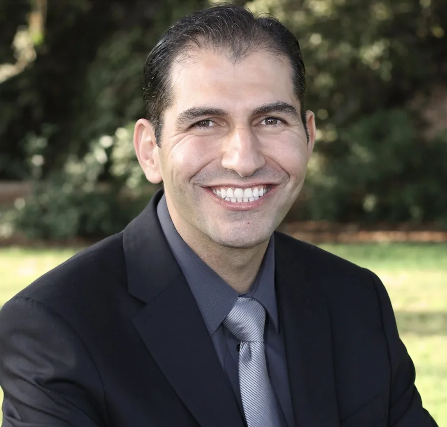 Portrait of Dr. Feras Al Rezk smiling, wearing a dark suit and tie